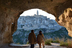 Two students stand under a stone archway and look out at an ancient city.